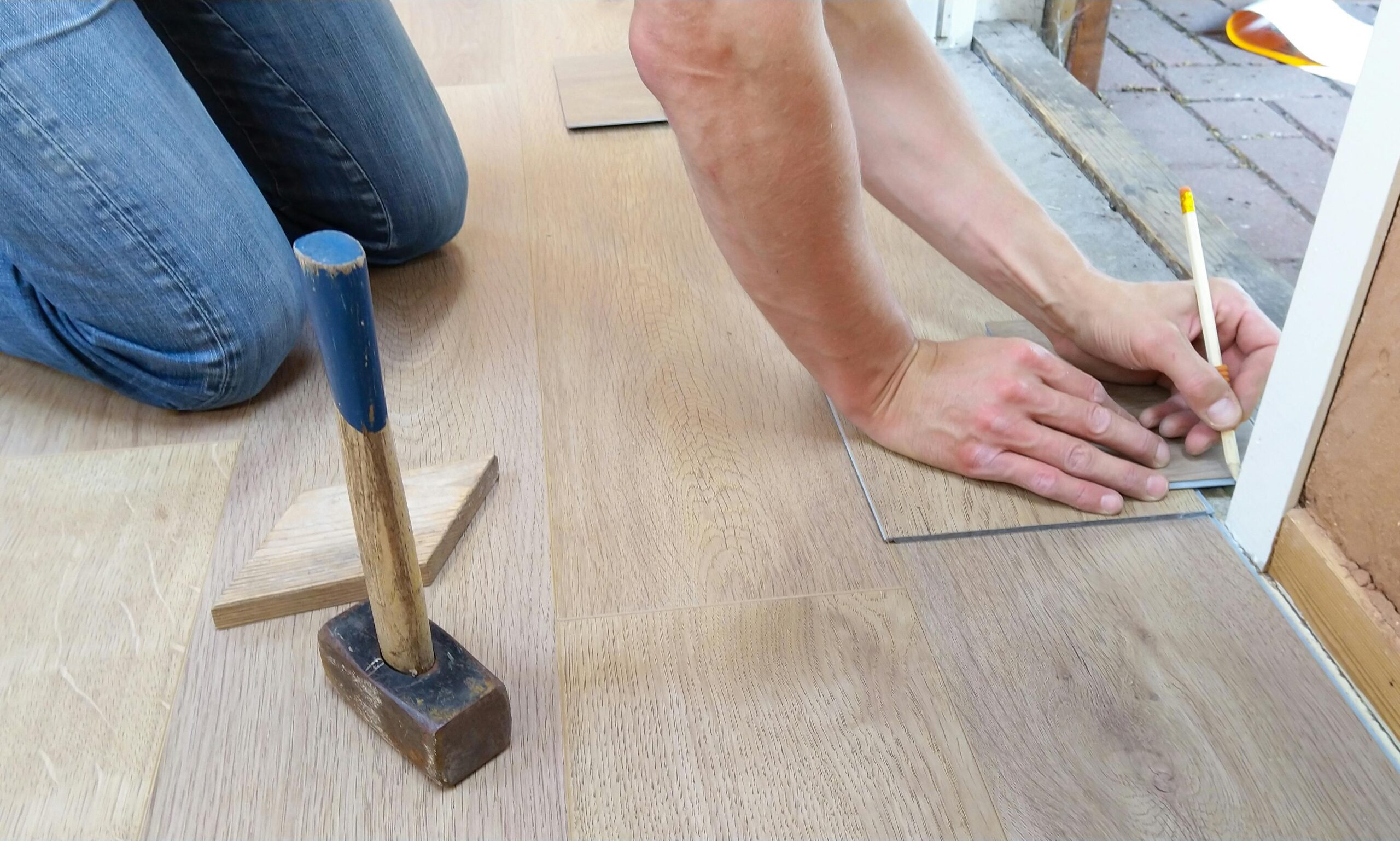 Person marking a tile for flooring installation with a pencil and mallet nearby.