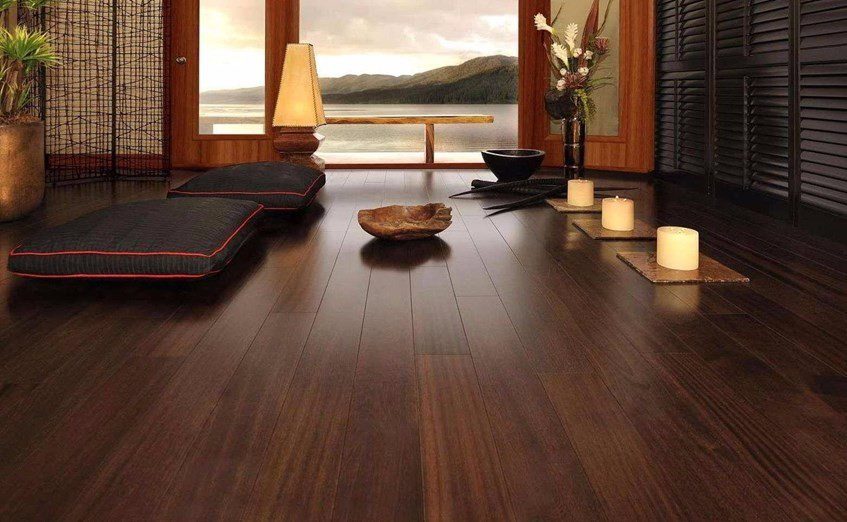 Serene room with dark wooden flooring, cushions, candles, and a view of nature.