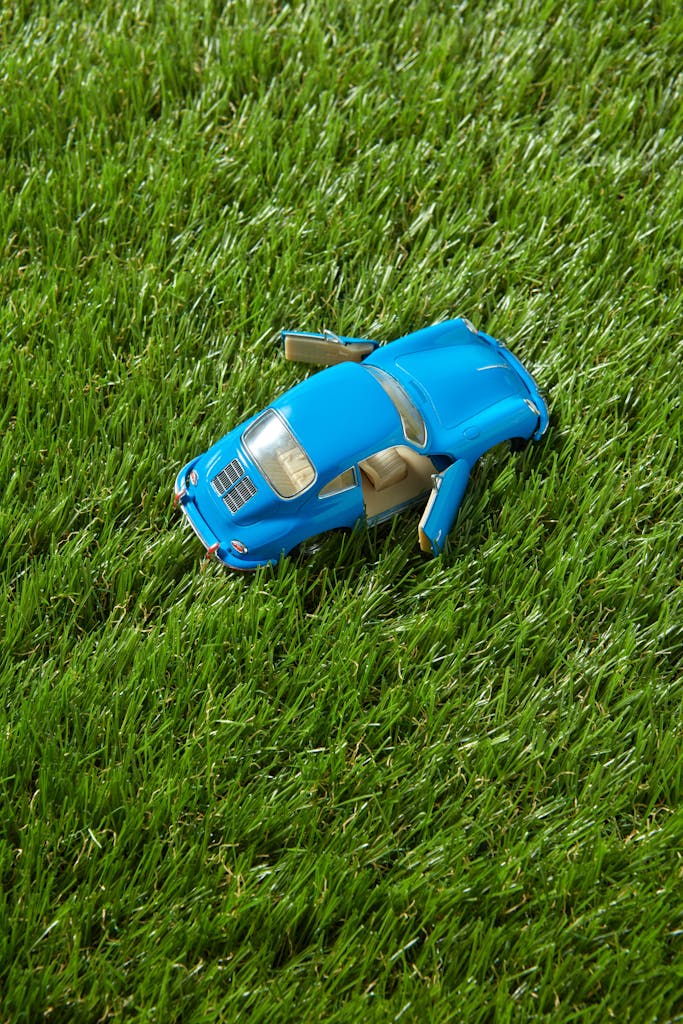 A blue toy car with open doors placed on vibrant green grass, captured close-up.