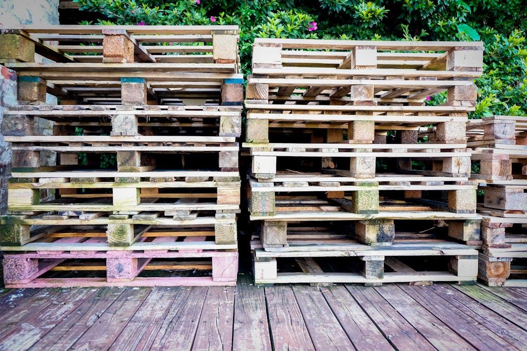 A pile of wooden pallets on a wooden deck surrounded by greenery, suitable for industry and recycling themes.