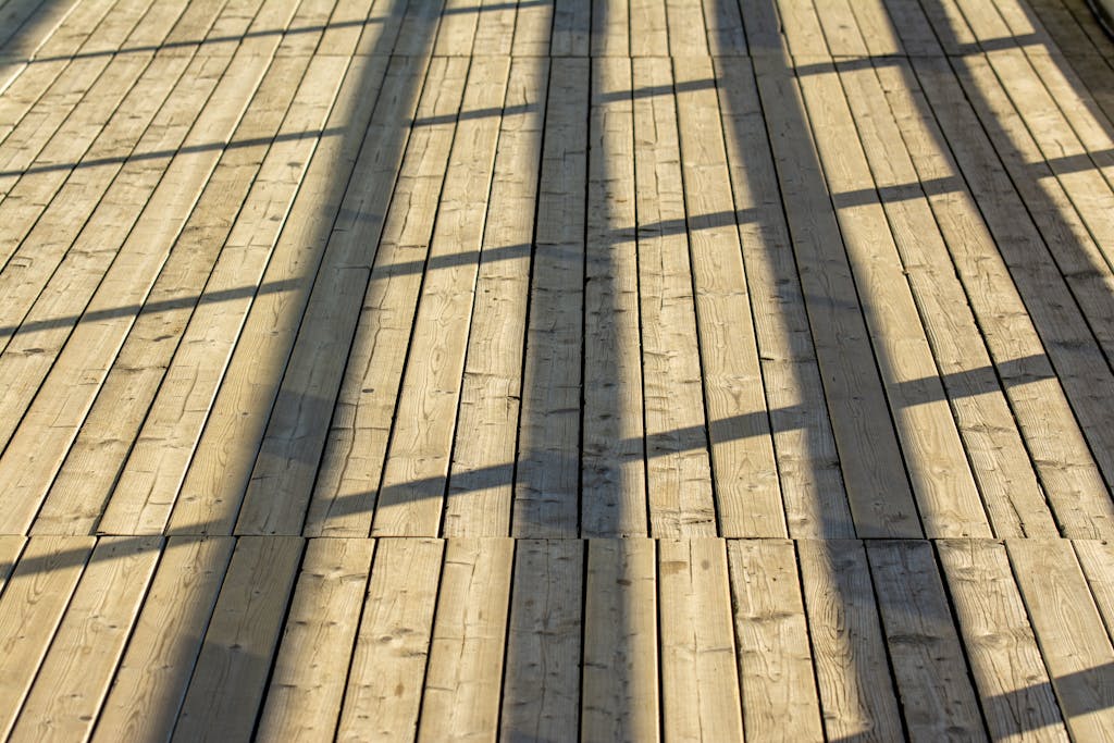 A wooden deck beautifully lit by sunlight, casting geometric shadows of a railing.