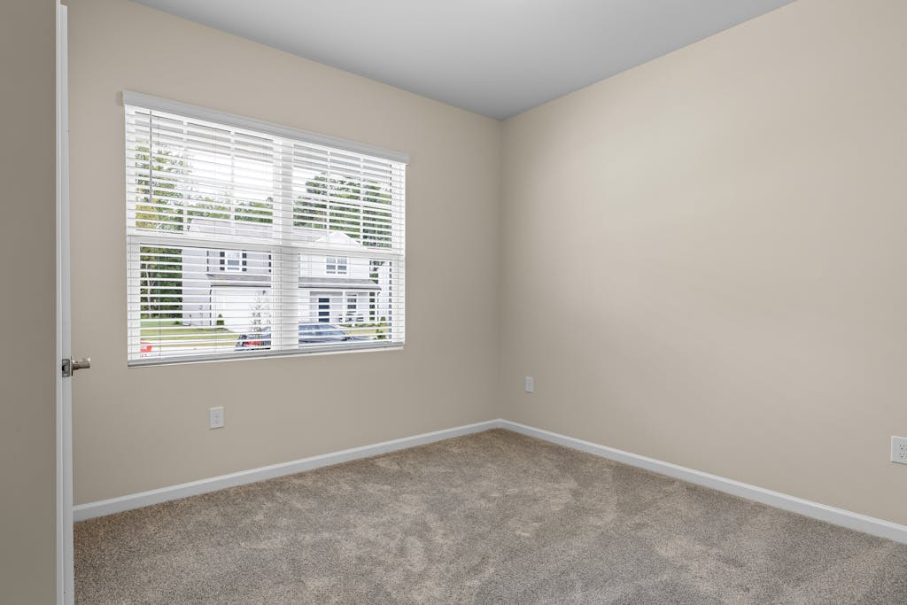 An unfurnished neutral-colored room with a large window, perfect for real estate listings.
