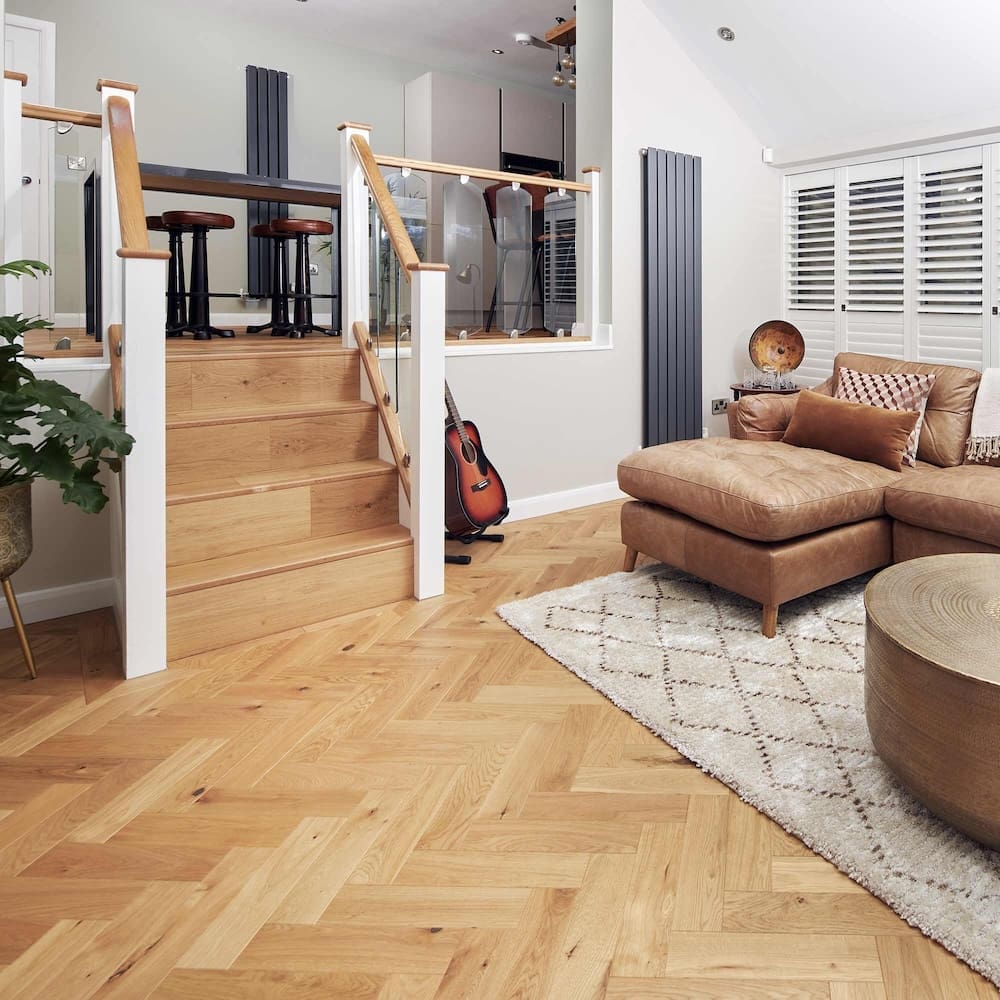 Living room with herringbone wood flooring, stairs, and modern furniture, including a leather sofa and a guitar.