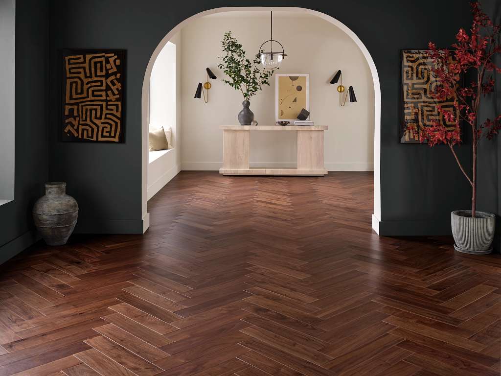Room with dark herringbone wood flooring, arched entryway, and modern decor including artwork and plants.