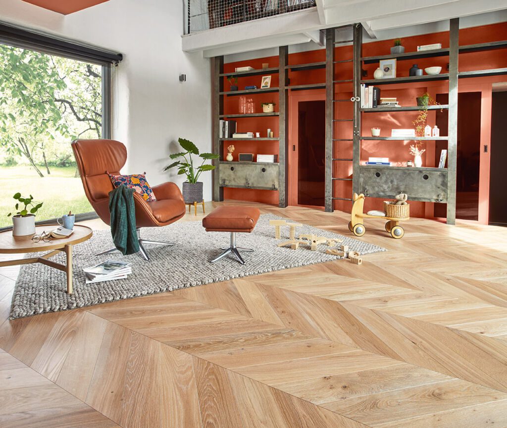 Living room with light herringbone wood flooring, a brown leather chair, and colorful shelves.