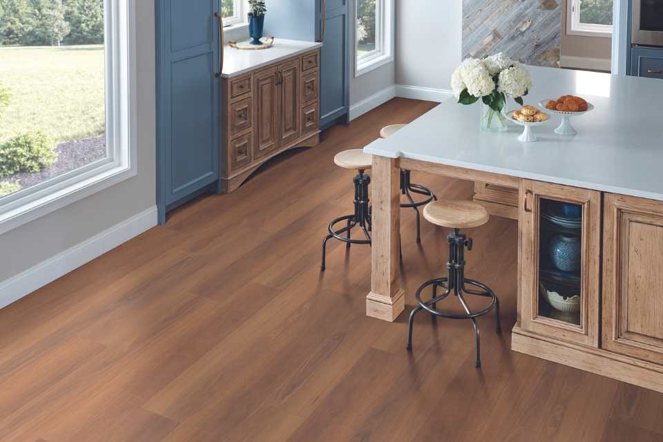 Kitchen with light wooden flooring, a white countertop, and wooden bar stools at the island.