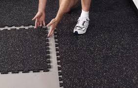 Person laying black rubber interlocking tiles on the floor for installation.