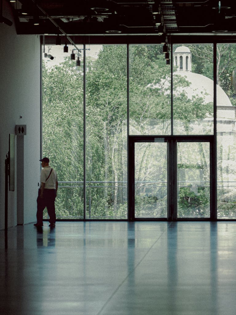 Side view of a man walking in a modern building with large windows overlooking greenery.