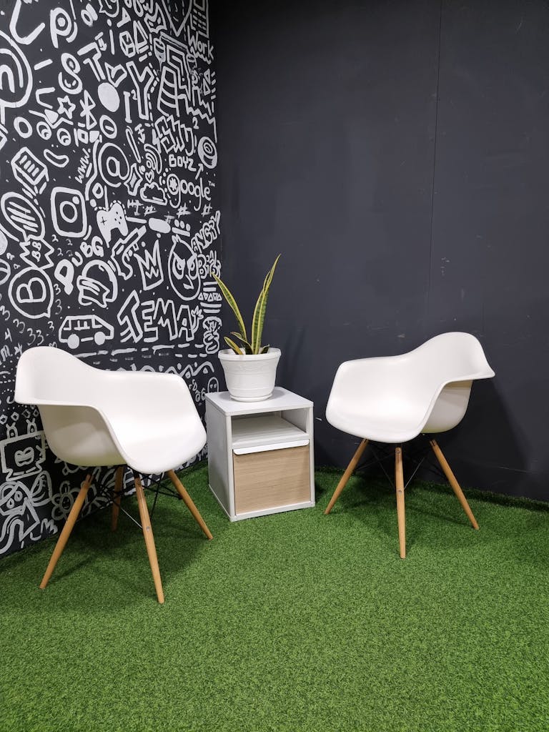 Two modern chairs with side table on artificial grass, graffiti wall backdrop.