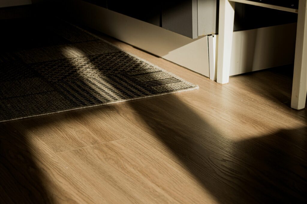 Wooden flooring with sunlight casting shadows over a textured rug, creating a cozy and inviting atmosphere.