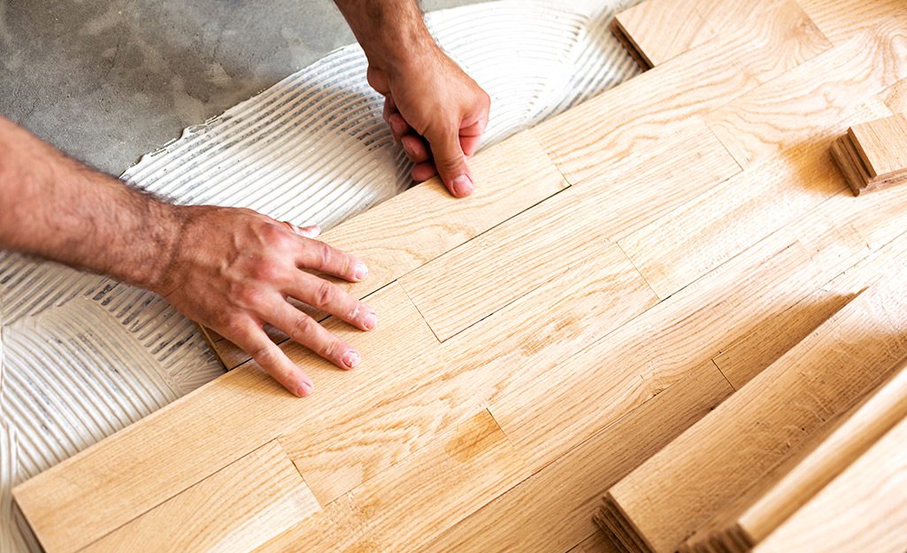 Person placing wooden floor planks on adhesive during installation.