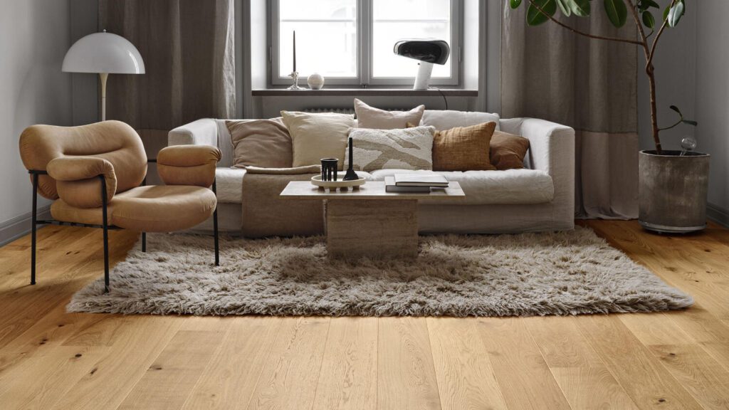 Living room with light hardwood flooring, a plush rug, a beige sofa, and modern decor.